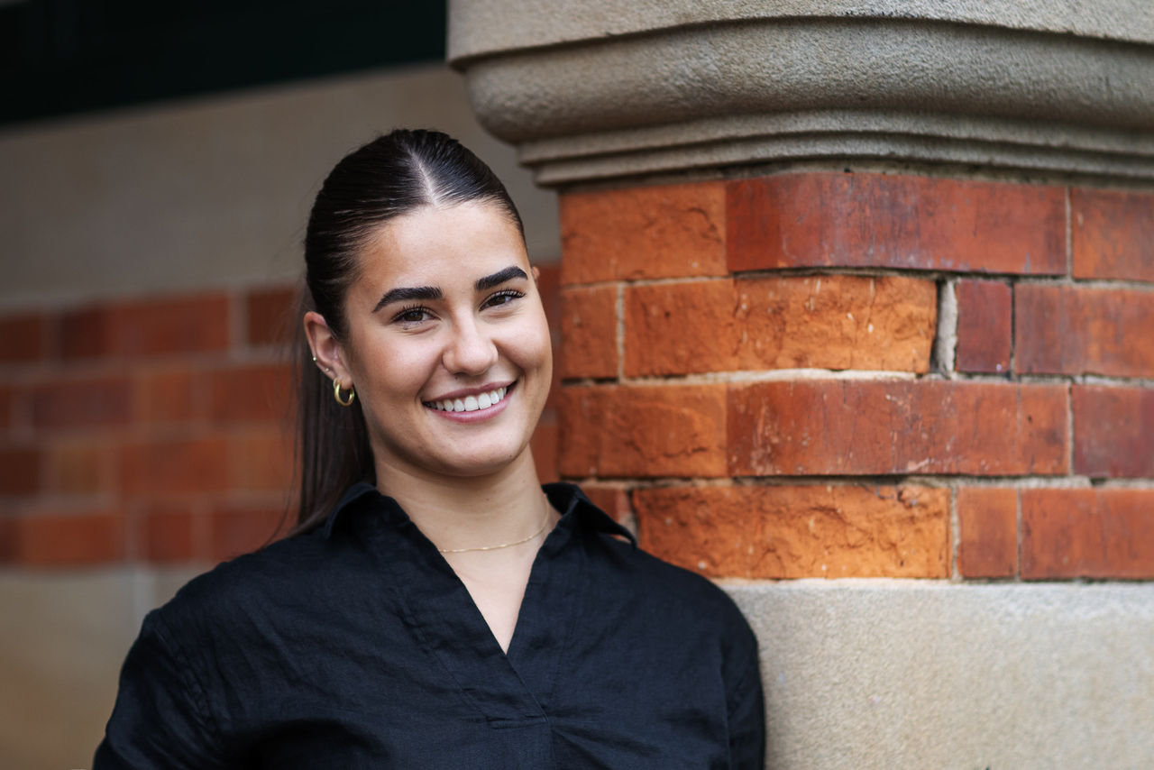 Female student with black shirt standing in front of brick wall.